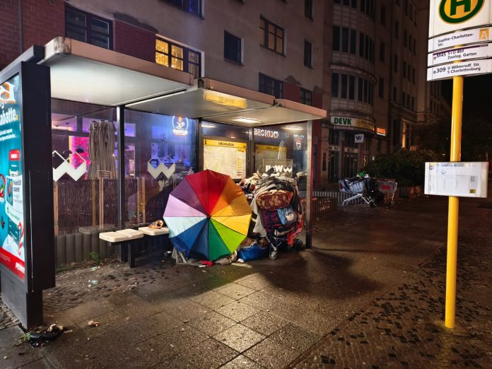 Kunterbunt an einer Bushaltestelle in der Migrantenmetropole Berlin. © Münzenberg Medien, Foto: Helmut Krüger, B: Frieder Fuchs, Ort und Datum der Aufnahme: Berlin, 8.12.2025
